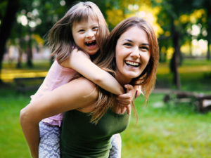 mother giving daughter piggy back in park
