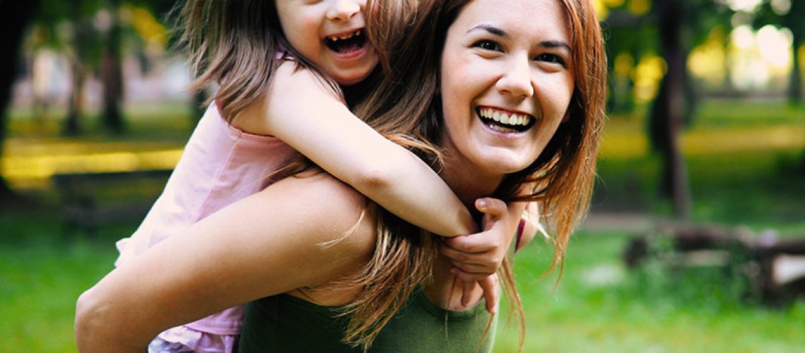mother giving daughter piggy back in park